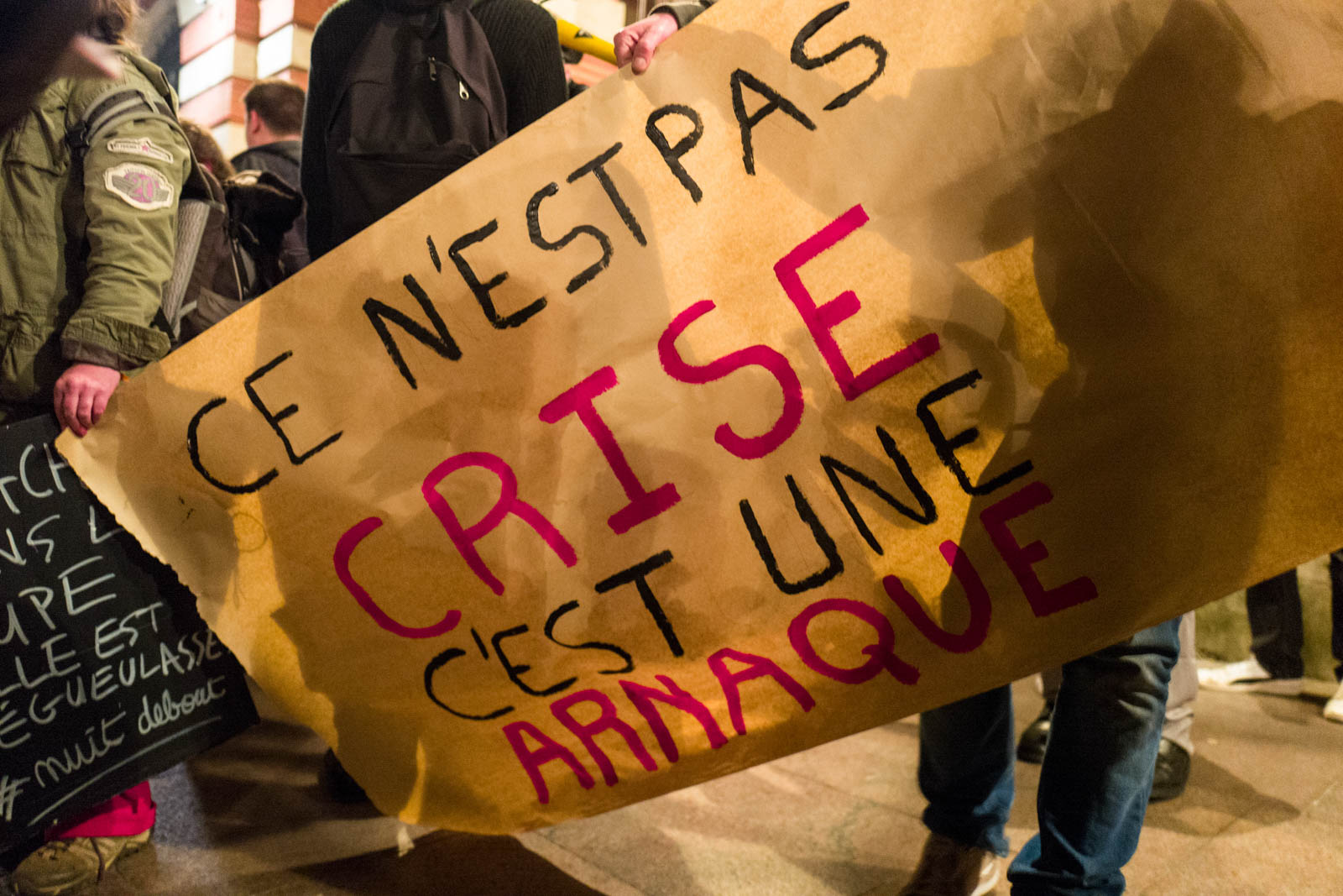 Affiche avec écrit Ce n'est pas une crise c'est une arnaque lors du rassemblement NUIT DEBOUT sur la place du Capitole. Depuis le 31 mars des personnes se sont installées sur différentes grandes places dans des villes de l'hexagone.  Ces rassemblements pacifiques, appellés NUIT DEBOUT sont ouverts et populaires, ils visent à réinvestir l’espace public pour échanger, débattre et construire, la Place du Capitole est occupée depuis le 5 avril. 6/04/2016, Toulouse-France.